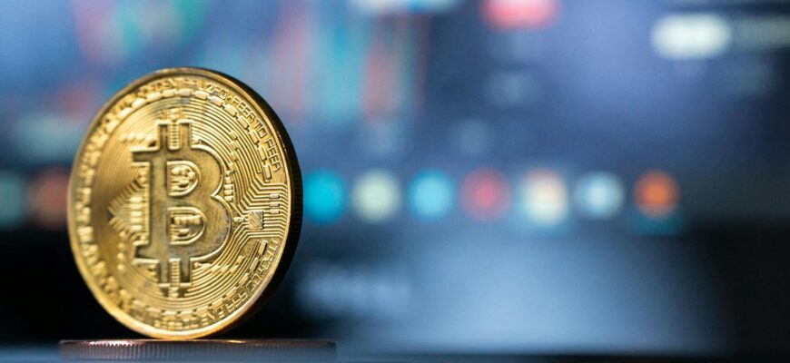 Gold Bitcoin coin with blurred financial chart in background, representing cryptocurrency trading.