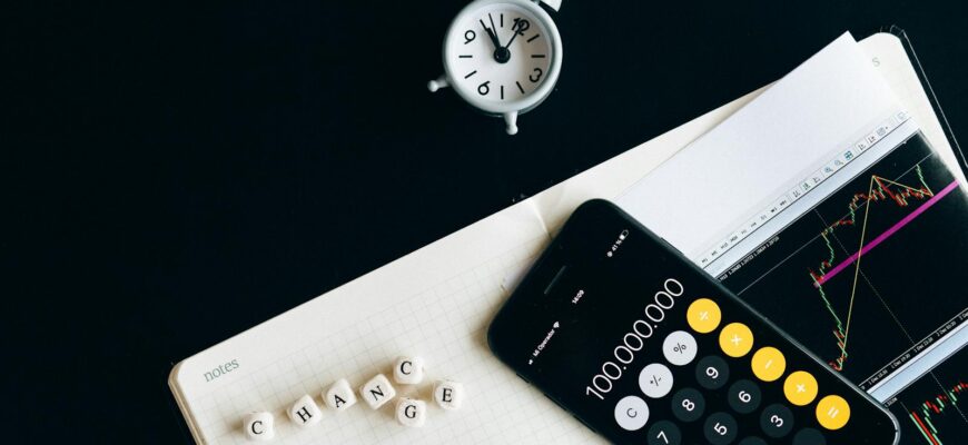 Notebook with an iPhone displaying 100,000,000, desk clock and financial charts suggesting market analysis.