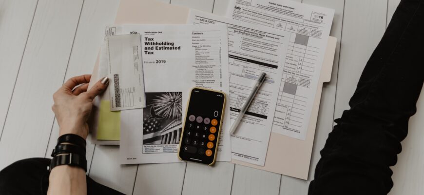 person holding paper near pen and calculator